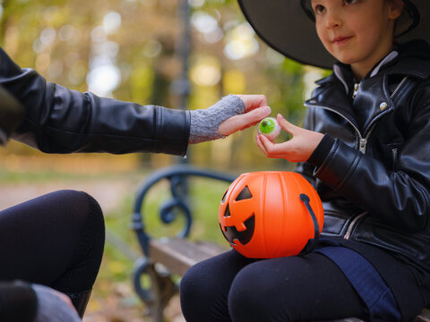 Mother and daughter prepare for Halloween walk in autumn park, wearing witch hats and holding jack o lantern, surrounded by colorful foliage in Zagreb in Croatia sunny October day.
