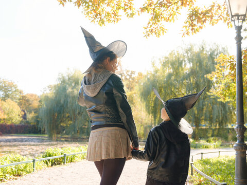Mother and daughter walk through autumn park during Halloween celebration, enjoying colorful foliage and seasonal atmosphere while spending quality time together outdoors.