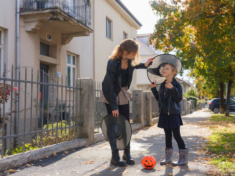 Mother and daughter go trick or treating down residential street during Halloween. Family holds pumpkin lanterns passing decorated autumn houses in Zagreb Croatia