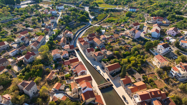 Peaceful waterfront of Vrboska features charming bridges, traditional stone houses and calm Adriatic Sea. Sunny summer day highlights authentic Mediterranean atmosphere of picturesque fishing village
