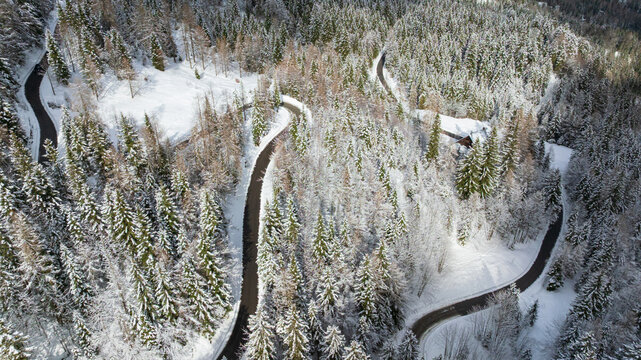 Drone captures majestic snow covered peaks and winding road in Triglav National Park. Traditional wooden cabin sits surrounded by frozen alpine pine forest near Vrsic Pass during winter day.