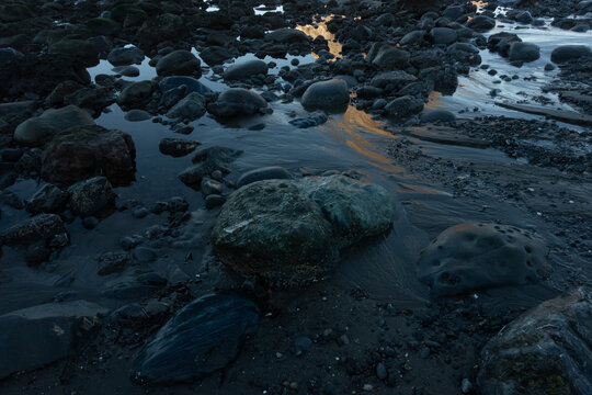 Moody low key photography of golden sunset reflections in rocky tide pools on an Oregon beach