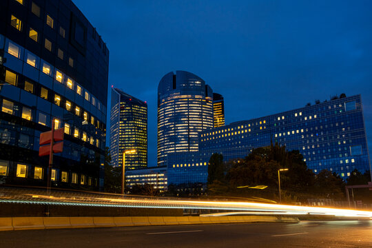 Office buildings illuminated at blue hour in La Defense, Paris, France, with light trails adding movement to the modern business district cityscape