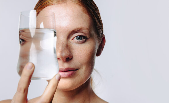 Woman holding glass of water over eye in studio