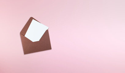 Brown paper envelope with a blank white card placed on a soft pink background. The minimalist stationery composition provides useful copy space and represents correspondence, invitations, greetings © Александра Алероева