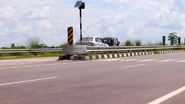 Dibrugarh, Assam, India &ndash; 23 September 2026: A three-wheeler travels along a modern highway beside roadside safety barriers and solar-powered equipment under a bright partly cloudy sky.