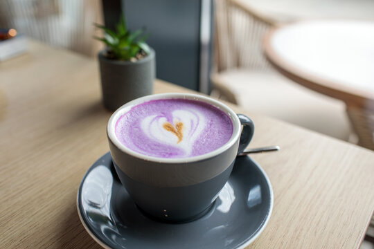 Purple ube latte with heart shaped latte art in dark ceramic cup on wooden cafe table, potted succulent nearby, soft natural light and cozy coffee shop atmosphere, high quality photo