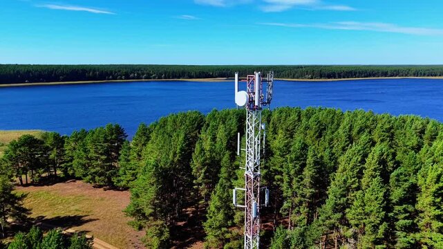 Telecommunication tower standing tall amidst vibrant green pine trees by a calm blue lake