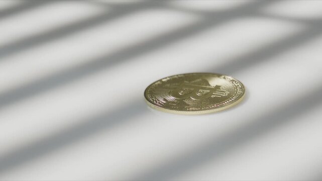 An older hand sets down a small stack of bitcoin coins on a white desk as window blind shadows stripe the scene in soft daylight.