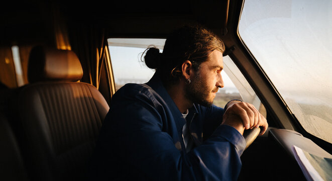 Contemplative man sits behind the wheel watching the coast at sunset