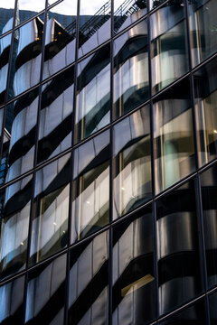 Curved dark glass office facade with repeating windows, showing modern architecture through reflections, geometric rhythm and abstract urban building detail