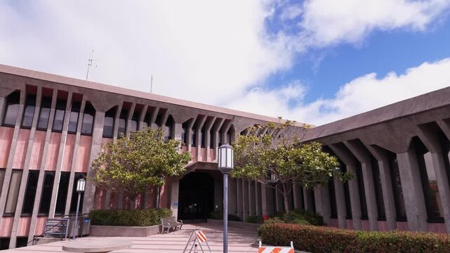 Panning shot of the exterior facade of the Daly City Hall building, a prominent civic government and administrative center located in San Mateo County under a beautiful blue sky with clouds