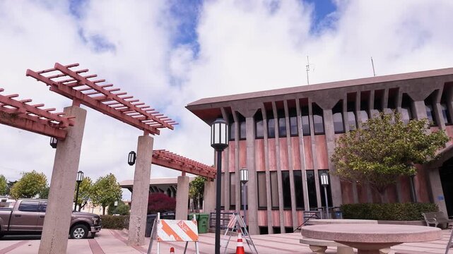 Modernist architecture of the City Hall building in Daly City, California, showing its distinctive concrete facade under a blue sky with soft white clouds, a quiet urban government setting