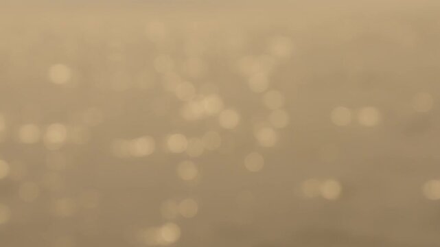 Abstract golden bokeh background with soft sunlight reflections on a shimmering surface. Warm beige and tan tones create a peaceful, out of focus atmosphere perfect for various design projects.