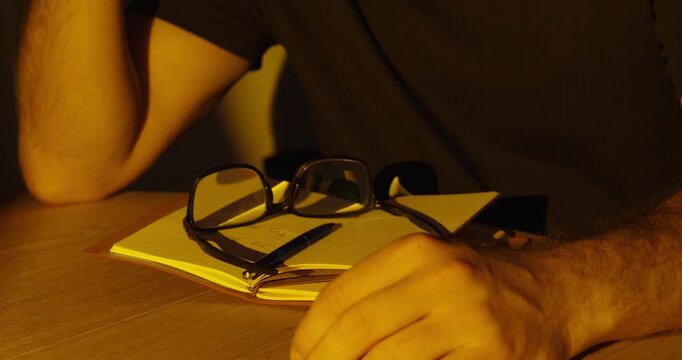 Close-up of eyeglasses falling onto a notebook in slow motion under warm dramatic cinematic lighting.