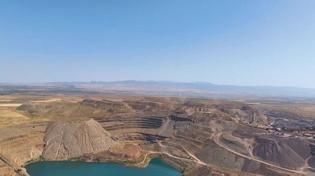 Aerial glides high above the mine's aquifer fed lake towards layers of terraced mine walls and slag heaps in Europe's largest open air iron ore mine Alquife Granada Province.