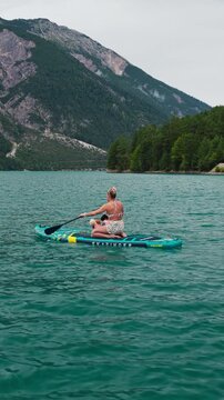Vertical Blonde Woman in Bikini Paddle Boarding with Dogs on Achensee Lake in Austrian Alpine Scenery