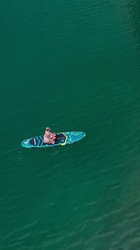 Vertical Aerial View of Blonde Woman Paddle Boarding with Dog on Blue Achensee Lake in Austrian Alps Top Overhead