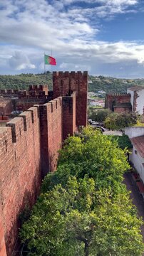 red sandstone walls of silves castle with portuguese flag waving under blue sky algarve portugal