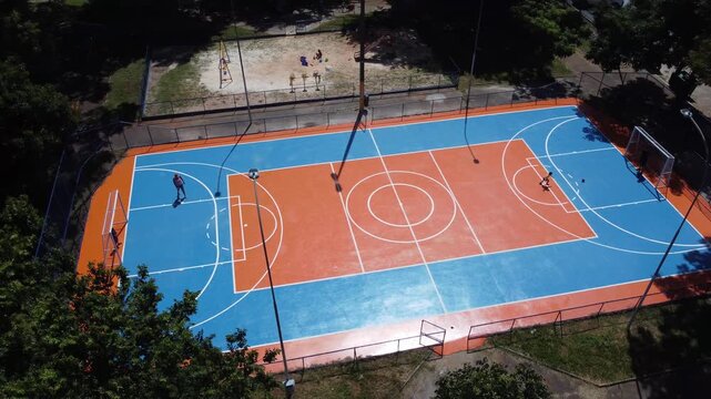 Brightly colored outdoor sports court in Brasilia, Brazil, with families using the public recreation facility surrounded by trees and open space, aerial view