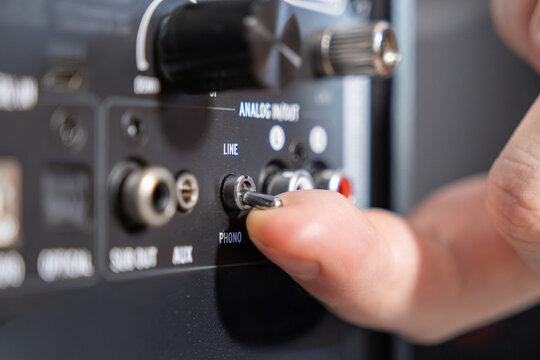 A finger flipping a toggle switch on an audio amplifier rear panel, adjusting the line or phono input setting to configure professional music equipment for high quality sound output
