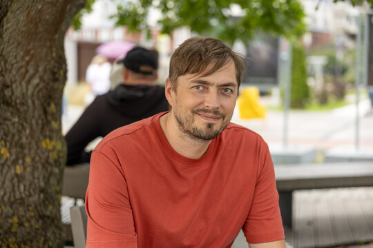 Smiling adult man in red T-shirt looking at camera while sitting outdoors