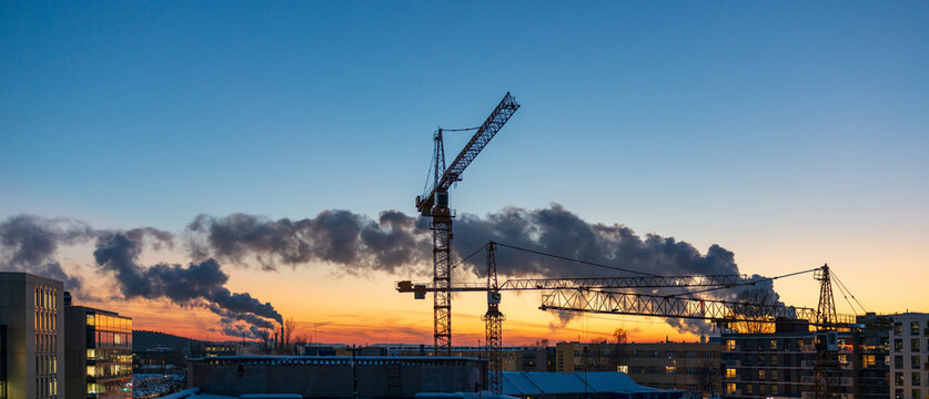 View of construction cranes silhouetted against a vibrant sunset sky over the urban landscape of Vilnius, Vilnius County, Lithuania.