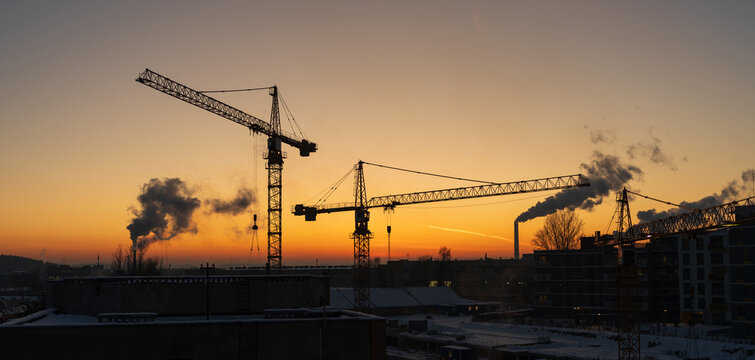 View of construction cranes silhouetted against a vibrant sunset sky over industrial buildings in Vilnius, Vilnius County, Lithuania.