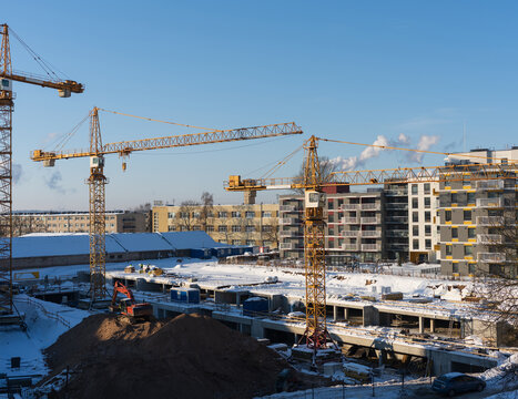 View of a construction site with yellow tower cranes, snow-covered ground, and modern apartment buildings under a clear blue sky in Vilnius, Vilnius County, Lithuania.