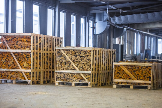 View of wooden crates filled with chopped firewood stacked inside a spacious industrial warehouse with large windows in Latvia.