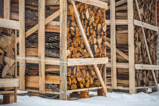 View of stacked firewood in wooden crates wrapped in plastic netting on a snowy ground in Latvia.
