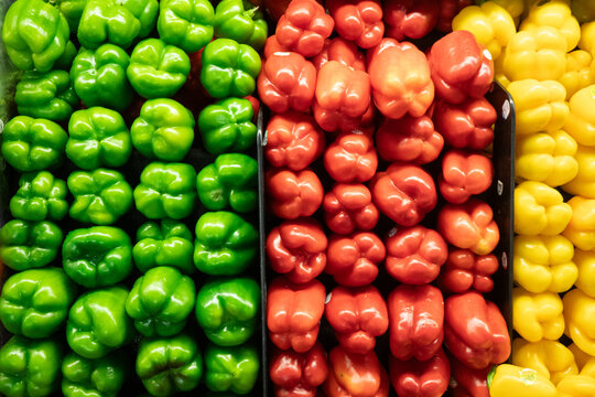 View of rows of fresh green, red, and yellow bell peppers neatly arranged in a grocery store display in California City, California, United States.