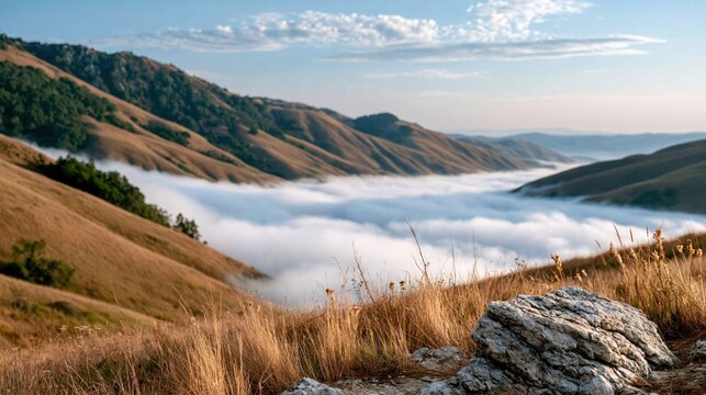 An awe-inspiring mountain landscape reveals rolling hills shrouded in mist, capturing the beauty of nature as the sun rises over the ethereal clouds below.