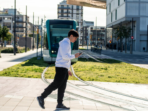 Young man walking distracted by smartphone near tram