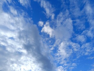 Fototapeta premium Bright blue sky with fluffy white clouds and a darker grey cloud mass. Daytime atmosphere