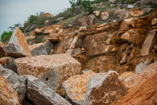 View of large granite boulders and rough stone fragments in a quarry, with a rocky hillside in the background in Jos North, Plateau, Nigeria.