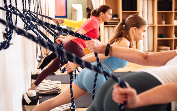 Group of diverse women engaged in fitness training, using resistance ropes in a bright studio, showcasing strength and teamwork in a dynamic workout environment