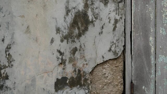 Weathered white plaster wall with cracked peeling stucco and exposed cement, rusty door hinge and old wooden door, grunge shabby texture background with copy space