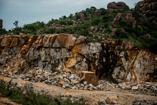 View of a rugged rock quarry with layered stone formations, scattered boulders, and green vegetation on the surrounding hills in Jos North, Plateau, Nigeria.