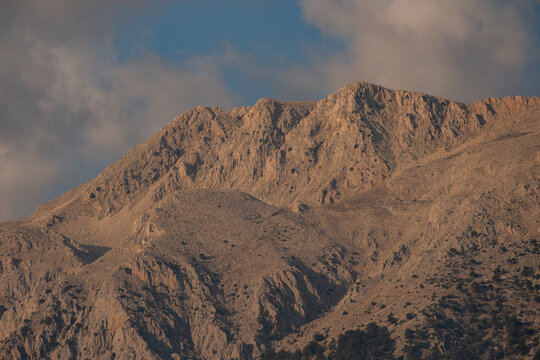 View of the rugged rocky slopes of a mountain peak illuminated by golden hour light under a soft sky in Fethiye, Mugla, Turkiye.