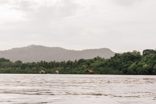 View of Raja Ampat with wooden stilt houses along the lush shoreline and mountains in the background in Southwest Papua, Indonesia.