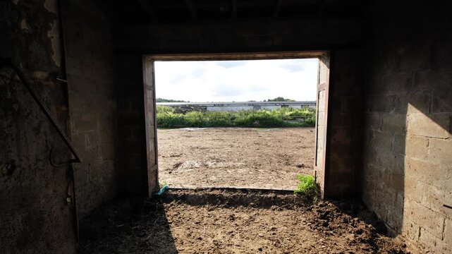 Farm building doorway looking out to a livestock enclosure and rural agricultural land