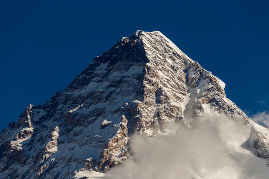 View of the majestic snow-covered peak of K2 rising against a deep blue sky with clouds at the base in Concordia k2 Base, Gilgit Baltistan, Pakistan.