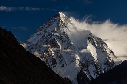 View of the snow-capped K2 mountain peak rising against a deep blue sky with wispy clouds and dramatic shadows at Concordia k2 Base, Gilgit Baltistan, Pakistan.