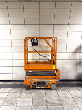 View of an orange scissor lift parked against a white tiled wall in a subway station in Istanbul, Istanbul, Turkiye.