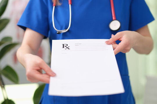 Healthcare worker in blue scrubs presents blank prescription paper with Rx symbol beside stethoscope, suggesting medical consultation, treatment planning, pharmacy service, patient documentation