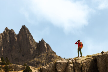 Fototapeta premium Hiker stands on a rocky cliff edge. They wear a red jacket and carry a backpack