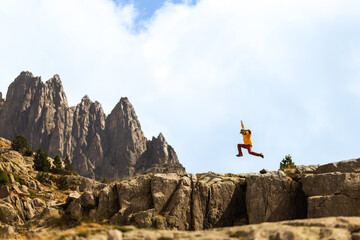 Person leaps over rocky cliff edge. Mountain peaks rise in distance. Clear sky frames the jump. Adventure spirit fills the moment. Perfect for travel or hiking themes © VICTOR