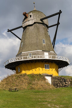 View of the historic Svanemollen windmill with its distinctive yellow base, wooden shingles, and surrounding grassy landscape in Kerteminde, Kerteminde Municipality, Denmark.