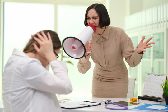 Angry aggressive female patient yells at doctor in clinic using megaphone. Conflicts at work in medicine concept